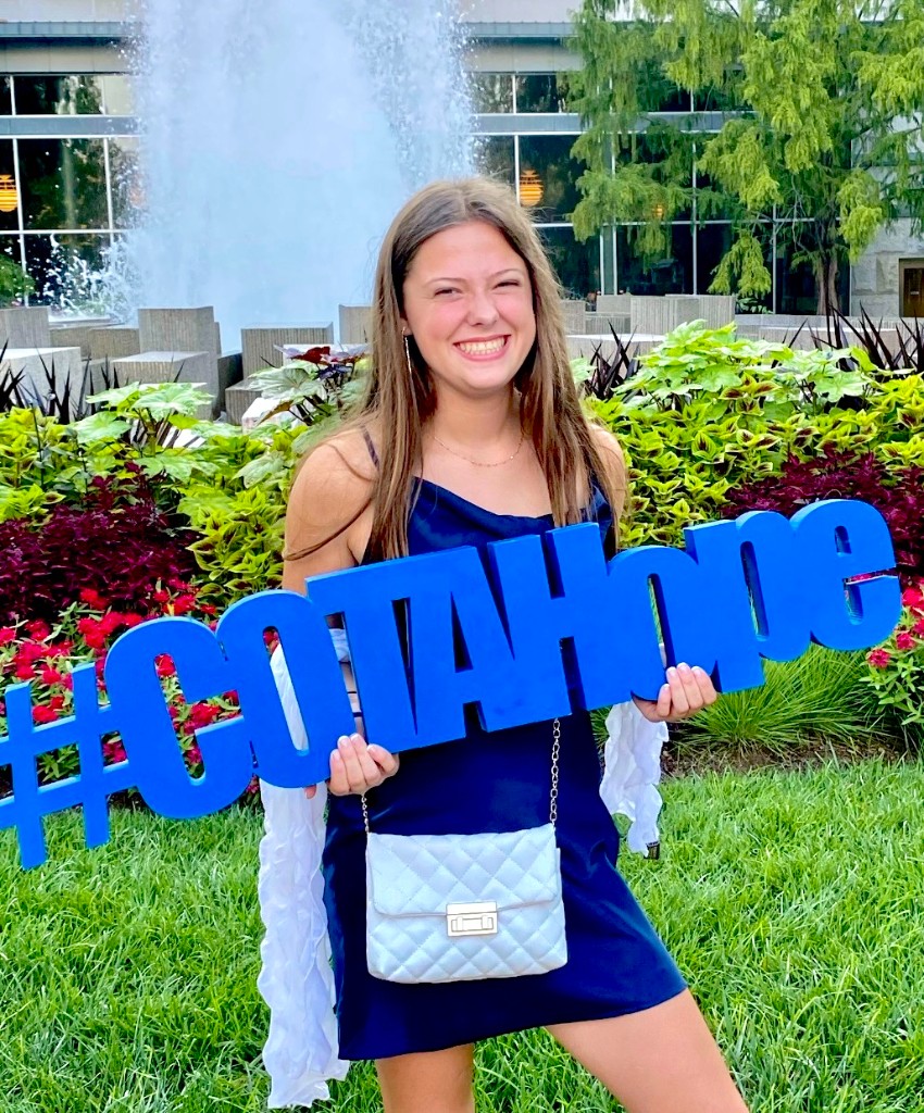 Clara Isaacs smiling outdoors with a #COTAHOPE sign